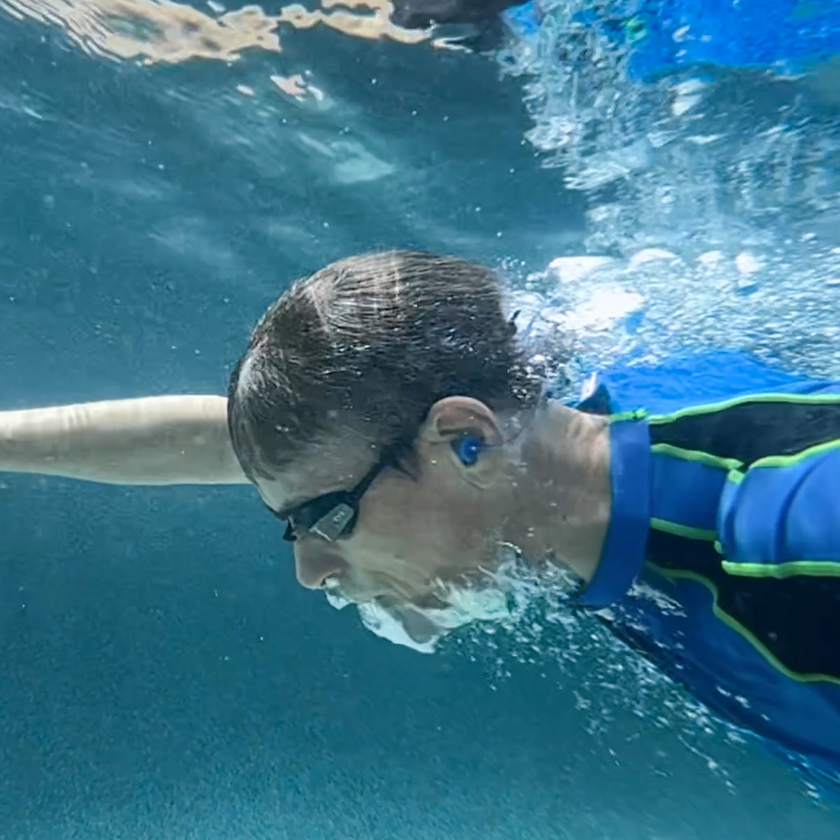 Swimmer underwater wearing blue Fluid earplugs
